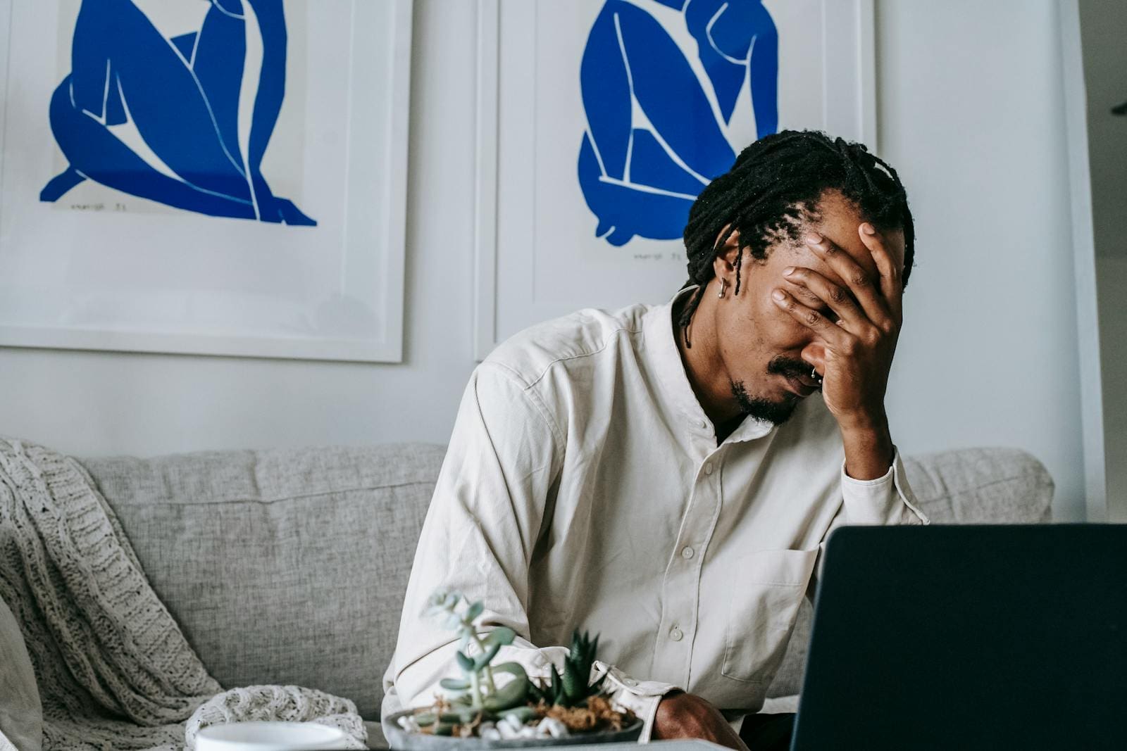 Photo by Alex Green Frustrated young bearded African American male freelancer with dreadlocks in casual shirt working on laptop at home and covering eyes with hand after failure